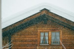 A close-up view of a rustic wooden cabin with snow-covered roof during a snowfall in winter.